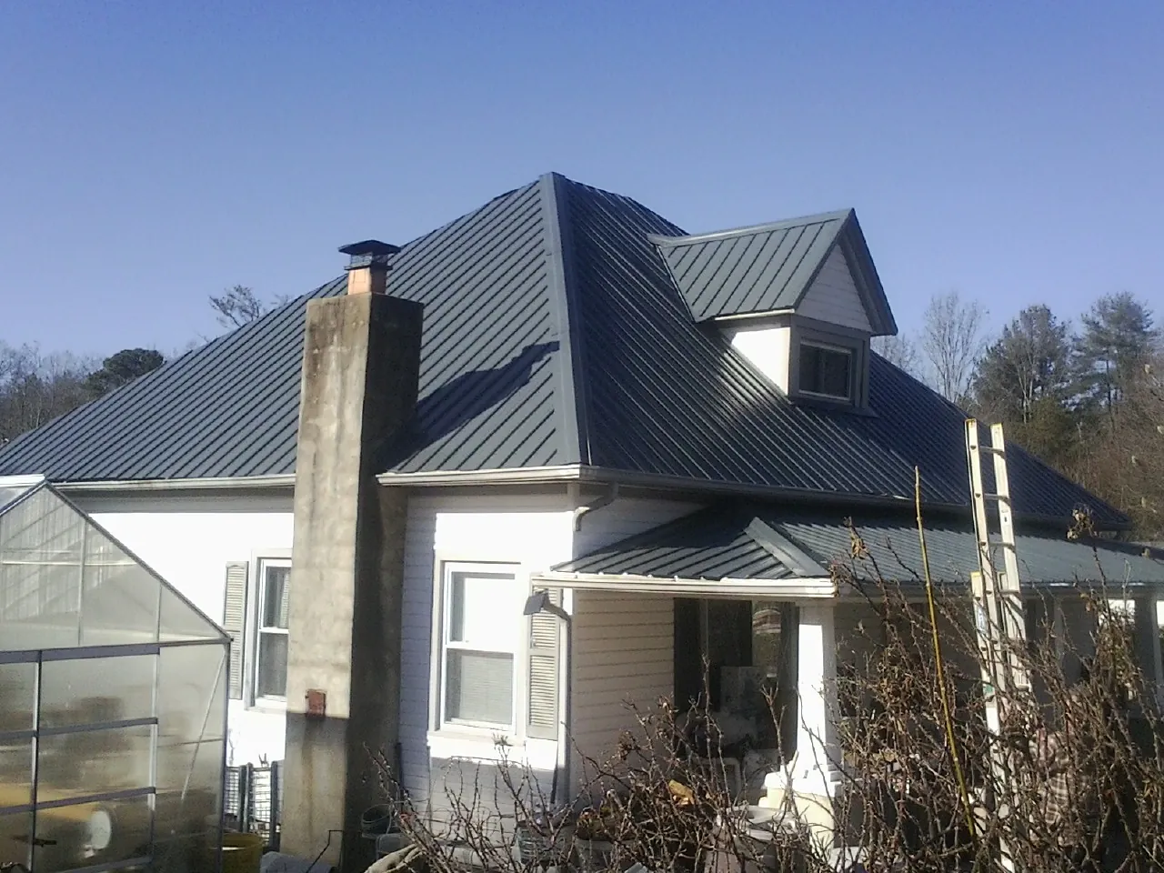 Dark blue standing seam metal roof on a white farmhouse with dormer — Slate & Tile Roof Repair by Roofing Brothers in Artesia