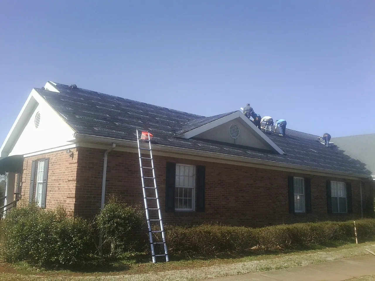 Crew tearing shingles off a brick ranch roof with a ladder set — Emergency Roof Repair work by our crew in Artesia