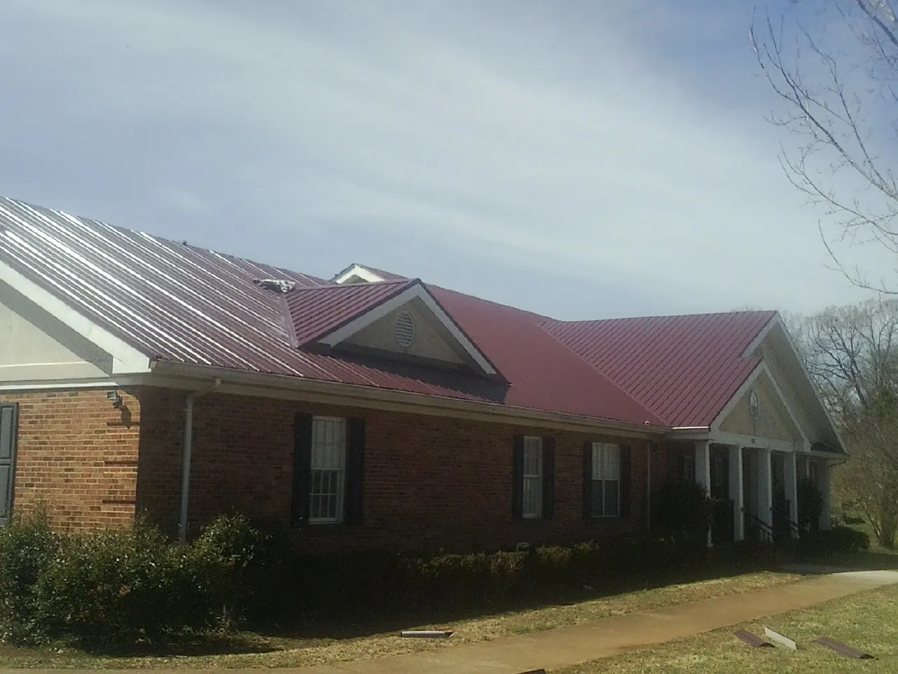 Red metal roof with gabled entries on a long brick building, from a Hail Damage Roof Repair job in Artesia