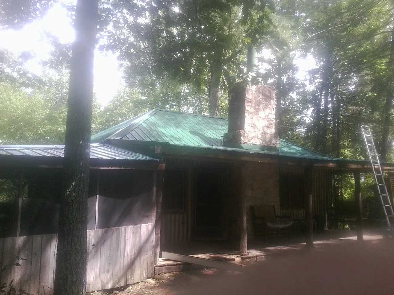 Green metal roof and stone chimney above a log cabin porch in Artesia